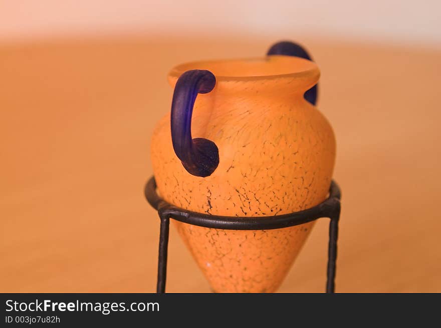 Greek vase close-up syle with blue and orange colors in a metal support on wood table