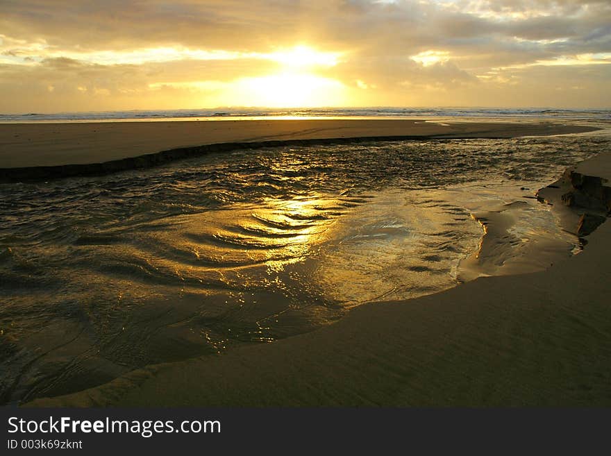 Texure and ripples on the top of a river of erosion running across a beach and into the ocean at sunset. Texure and ripples on the top of a river of erosion running across a beach and into the ocean at sunset.