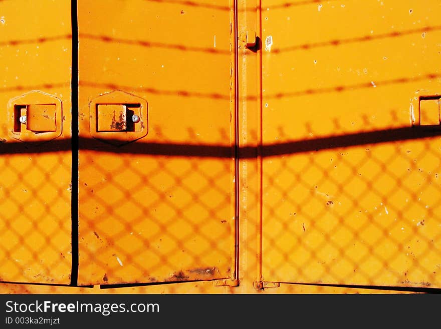 Yellow doors in an industrial stock yard showing silhouettes of barbed wire and chain link fence. Yellow doors in an industrial stock yard showing silhouettes of barbed wire and chain link fence.