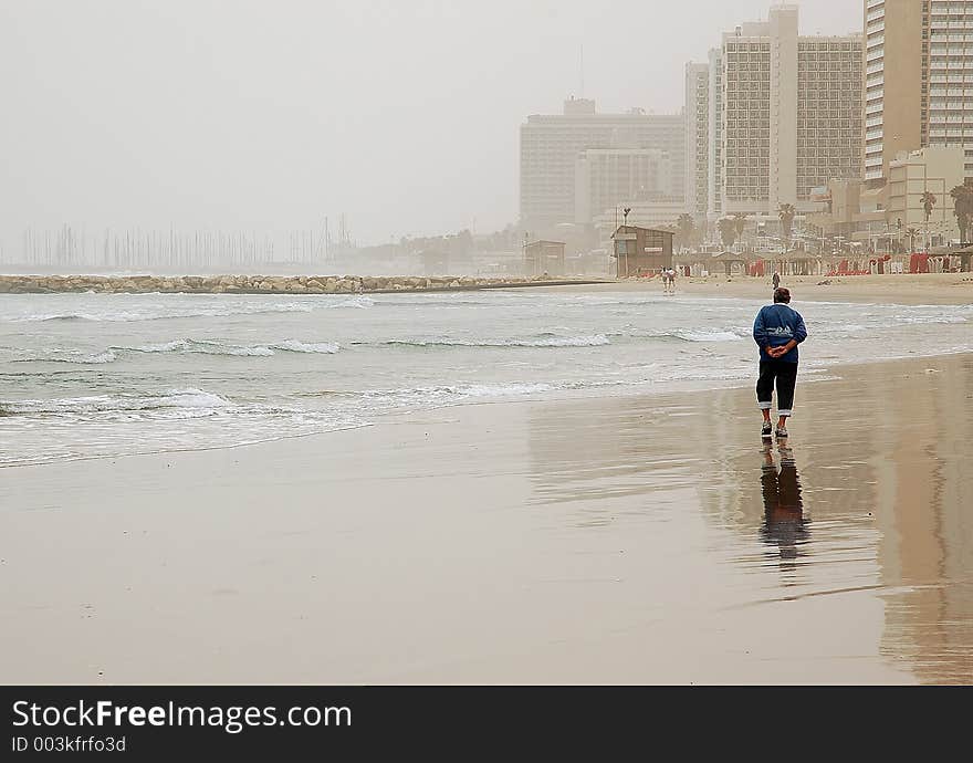 Elderly man enjoying a walk on empty winter beach in bad weather. Elderly man enjoying a walk on empty winter beach in bad weather