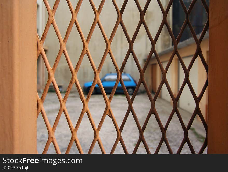 An out of focus renault 5 seen through a metal meshed gate