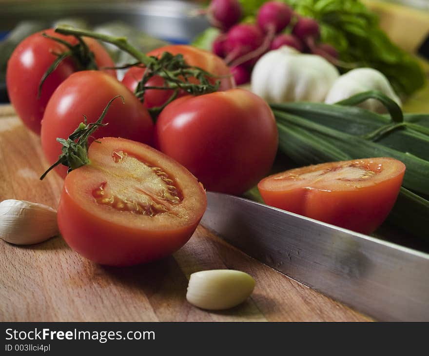 Cutting Tomatoes at kitchean board, vegetables at background. Cutting Tomatoes at kitchean board, vegetables at background