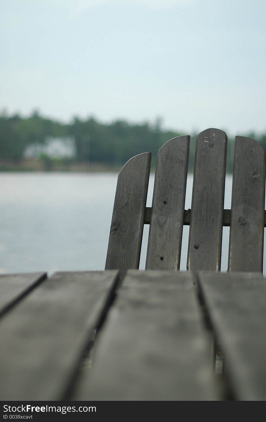 Adirondack chair hiding behind table . Focus is on the chair, with cottage in background. Adirondack chair hiding behind table . Focus is on the chair, with cottage in background