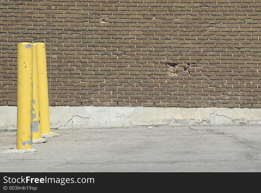 Yellow parking poles in a parking lot against a brick wall. Yellow parking poles in a parking lot against a brick wall.