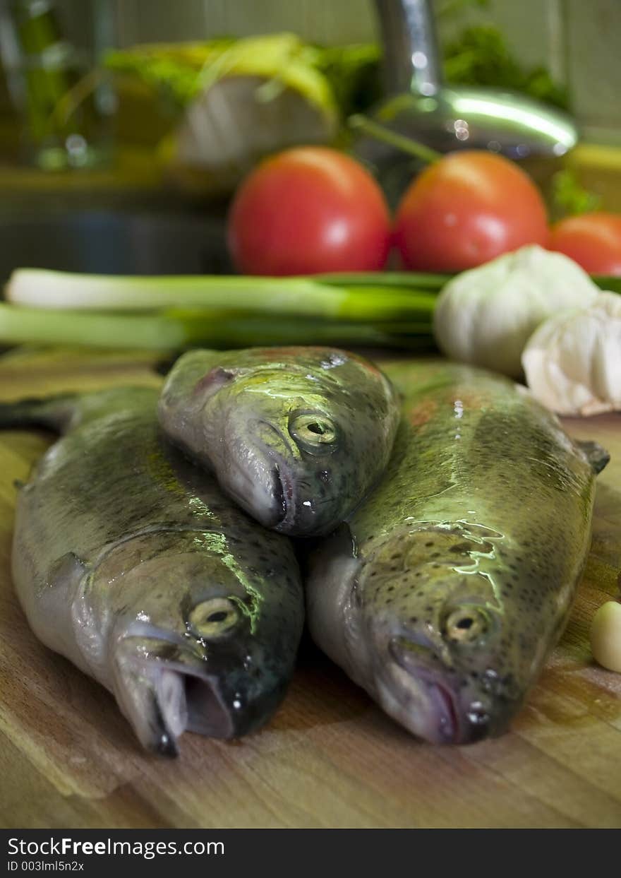 Three fresh trouts at kitchen cutting board, vegetables at background. Three fresh trouts at kitchen cutting board, vegetables at background