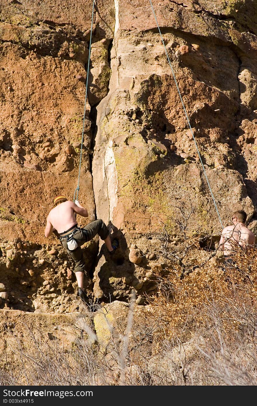 A pair of shirtless climbers work a granite wall in a state park in Colorado. A pair of shirtless climbers work a granite wall in a state park in Colorado