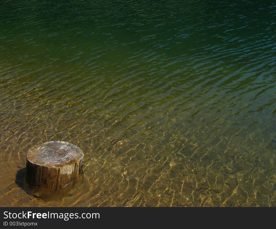 Shallow water of the mountain lake with a tree-stump in the foreground