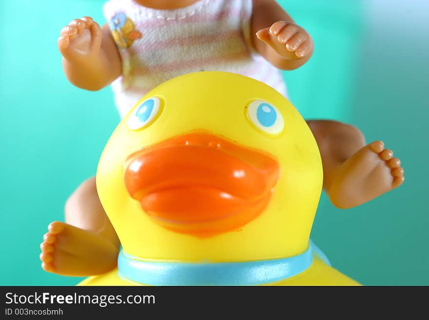 A yellow rubber ducky & doll close-up with a torquoise background in a turquoise bath basin. An imaginative childhood concept. Ideas, fun happiness imagination, domestic life togetherness. A yellow rubber ducky & doll close-up with a torquoise background in a turquoise bath basin. An imaginative childhood concept. Ideas, fun happiness imagination, domestic life togetherness