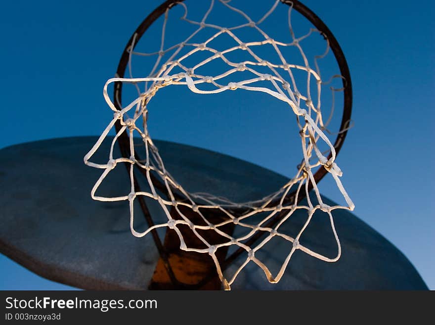 A rusty old basketball hoop against a blue sky in the evening.