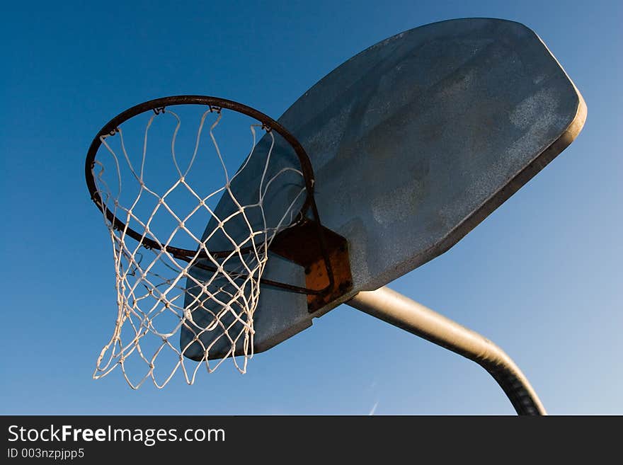 A rusty old basketball hoop against a blue sky in the evening.