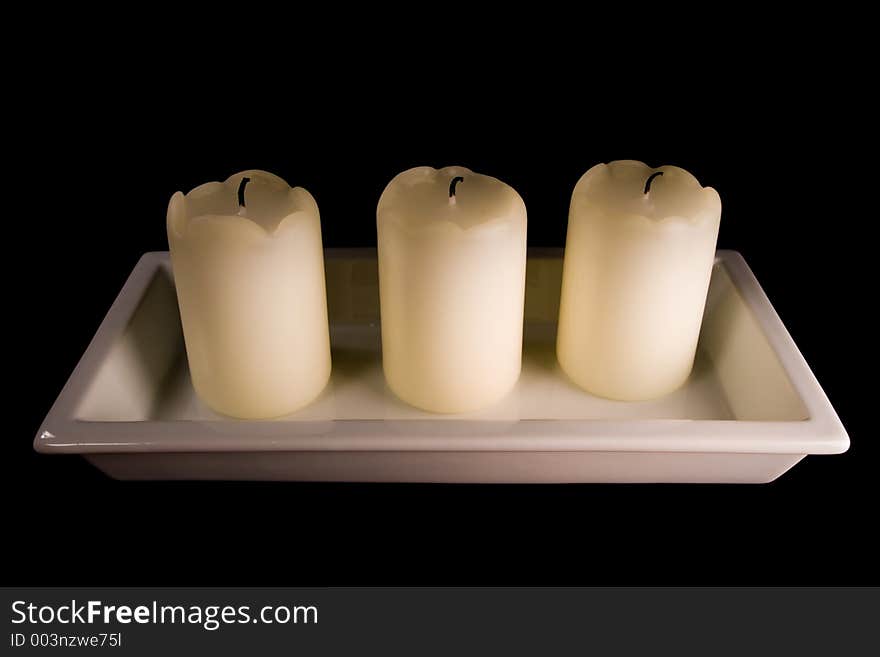 Three white candles lined up in a white saucer isolated on black. Three white candles lined up in a white saucer isolated on black