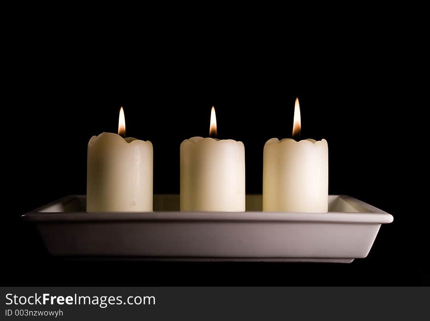 Three white candles lined up in a white saucer isolated on black. Three white candles lined up in a white saucer isolated on black