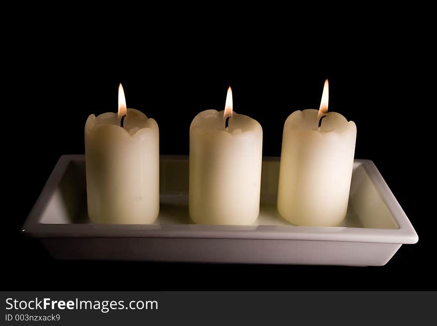 Three white candles lined up in a white saucer isolated on black. Three white candles lined up in a white saucer isolated on black