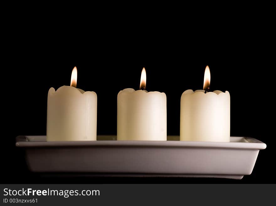 Three white candles lined up in a white saucer isolated on black. Three white candles lined up in a white saucer isolated on black