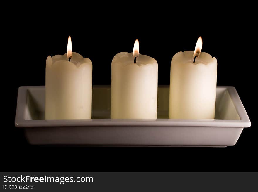 Three white candles lined up in a white saucer isolated on black. Three white candles lined up in a white saucer isolated on black