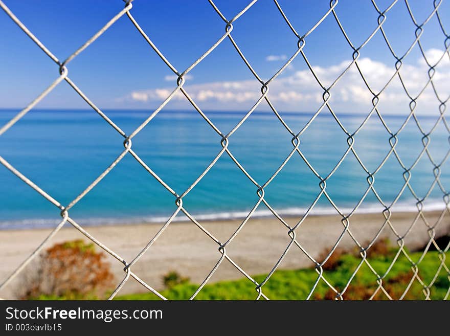 Beautiful paradise beach seen through wires of a fence