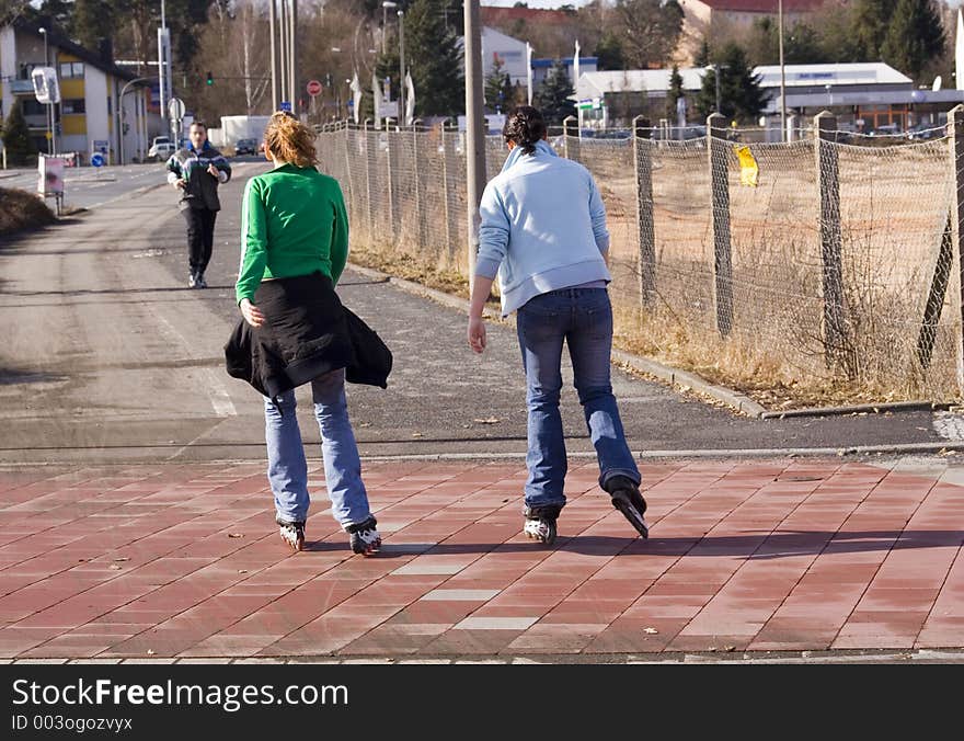 Two young girls skating in the morning. A man jogging in opposit direction. Two young girls skating in the morning. A man jogging in opposit direction.