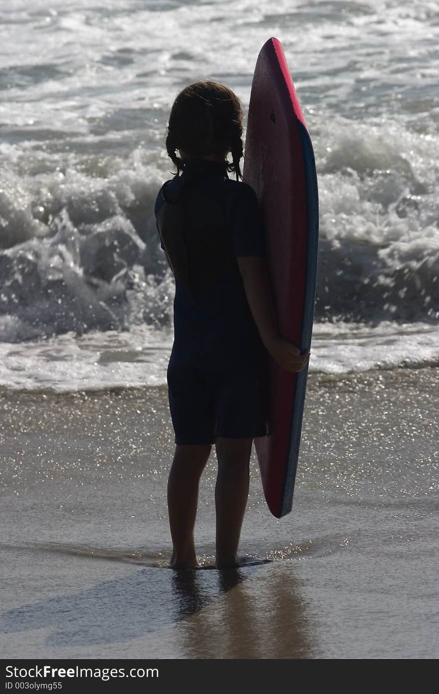 A young girl contemplates the ocean in front of her, as she clutches her boogie board. She is silhouetted by the late afternoon sun. A young girl contemplates the ocean in front of her, as she clutches her boogie board. She is silhouetted by the late afternoon sun.