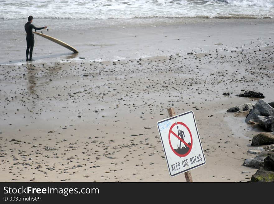 Man preparing to surf, warning sign in the foreground. Man preparing to surf, warning sign in the foreground