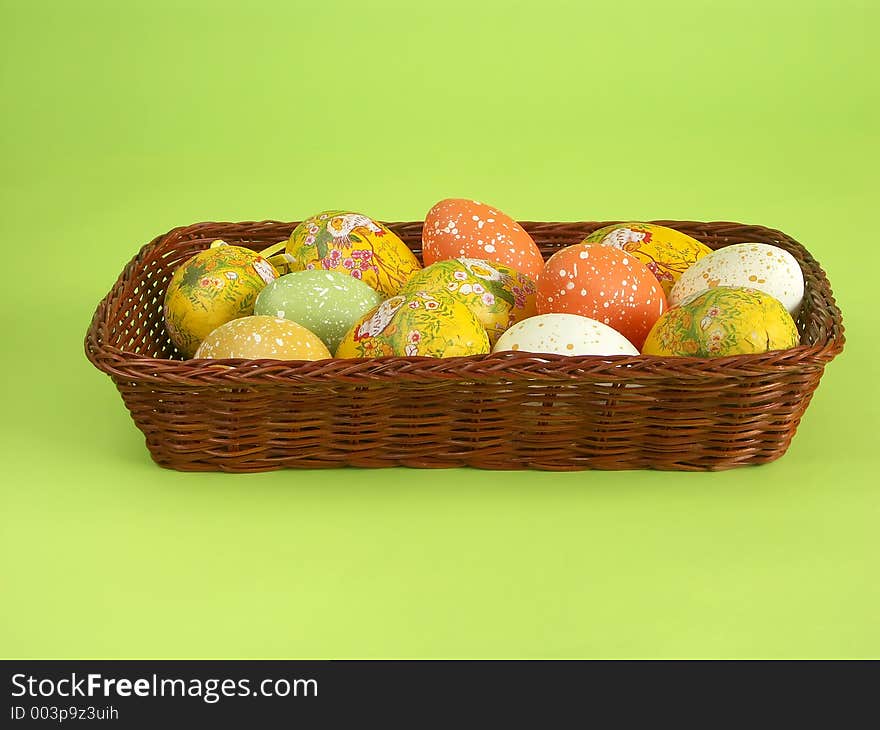 Wicker basket with Easter eggs over light green background. Wicker basket with Easter eggs over light green background