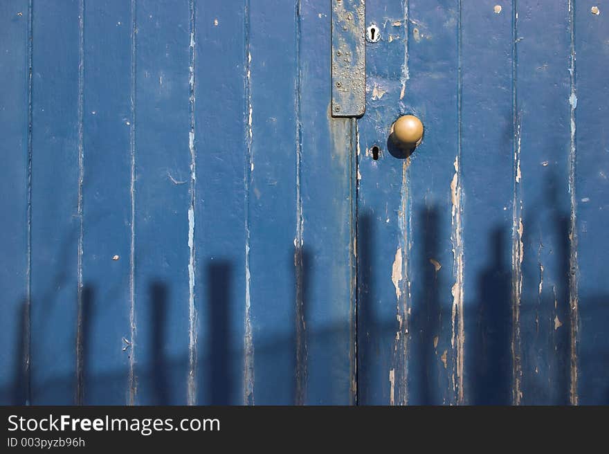 Background image of a blue door - cracked paint & shadows of a picket fence across the lower half of the image. Background image of a blue door - cracked paint & shadows of a picket fence across the lower half of the image