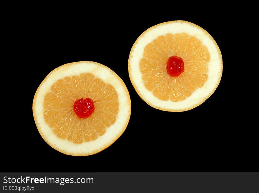 Two grapefruit halves with a red cherry at the centre of each, isolated on a black background. Two grapefruit halves with a red cherry at the centre of each, isolated on a black background.