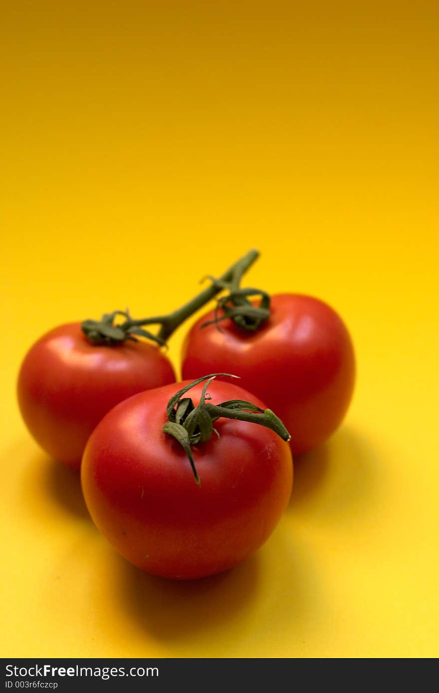 Three fresh and ripe tomatoes against yellow background, Great for advertisement!. Three fresh and ripe tomatoes against yellow background, Great for advertisement!