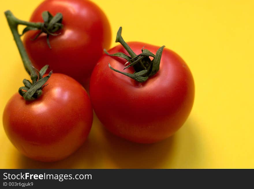 Three fresh and ripe tomatoes against yellow background, Great for advertisement!. Three fresh and ripe tomatoes against yellow background, Great for advertisement!