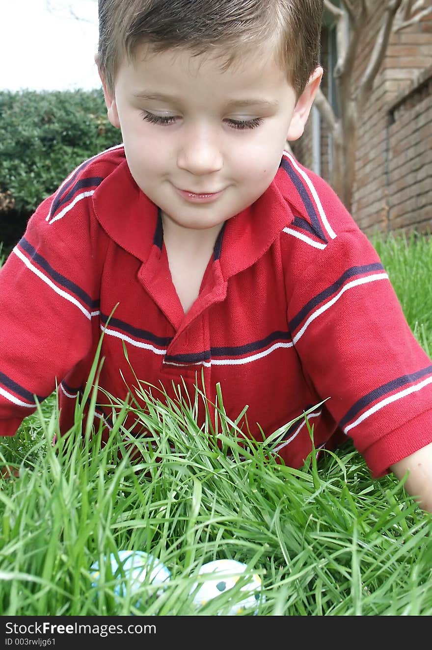 A young boy leaning over decorated Easter eggs he has found in the grass. A young boy leaning over decorated Easter eggs he has found in the grass.