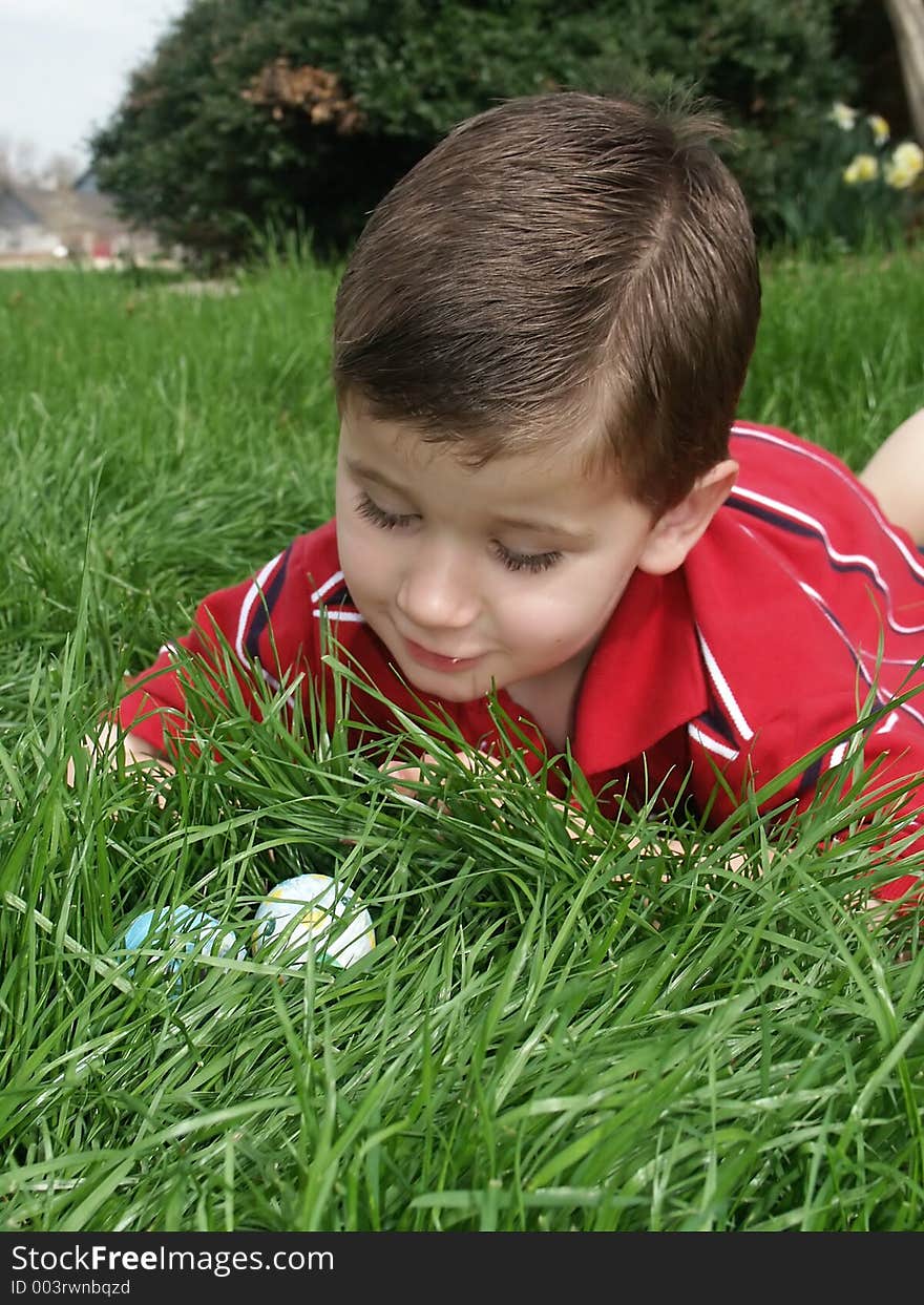 A young boy looking at Easter eggs he has found in the grass. A young boy looking at Easter eggs he has found in the grass.