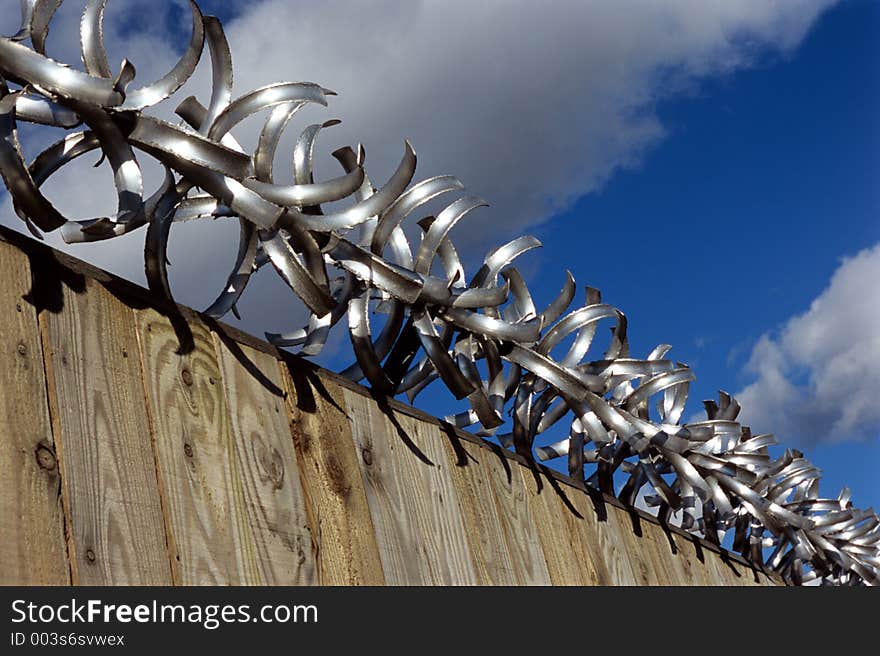 Razor wire on top of fence against a blue sky. Razor wire on top of fence against a blue sky.