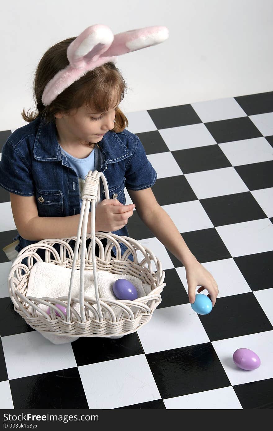 Little girl in Easter bunny ears picking up eggs and putting them in a basket. Little girl in Easter bunny ears picking up eggs and putting them in a basket.