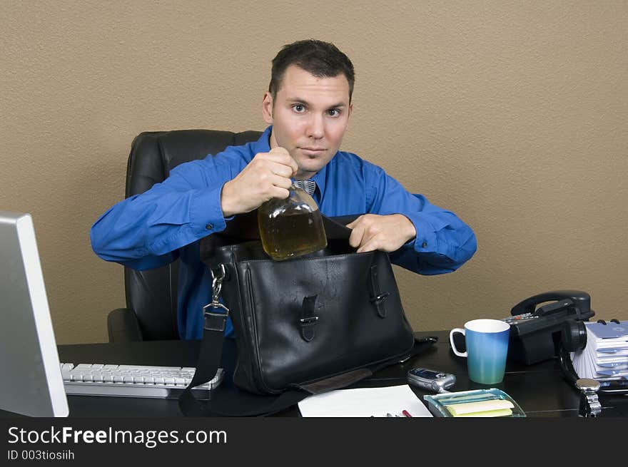 Employee smuggling some whiskey at his office in the working hours, happy about being able to pass through unnoticed. Employee smuggling some whiskey at his office in the working hours, happy about being able to pass through unnoticed