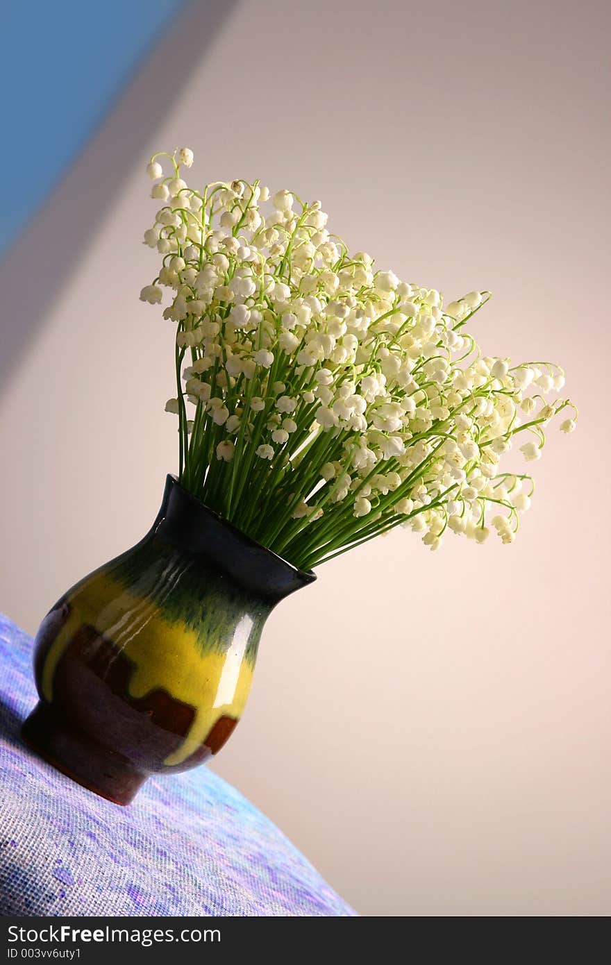 A vase with forest flowers of lilies on the valley standing on the inclined surface. A vase with forest flowers of lilies on the valley standing on the inclined surface