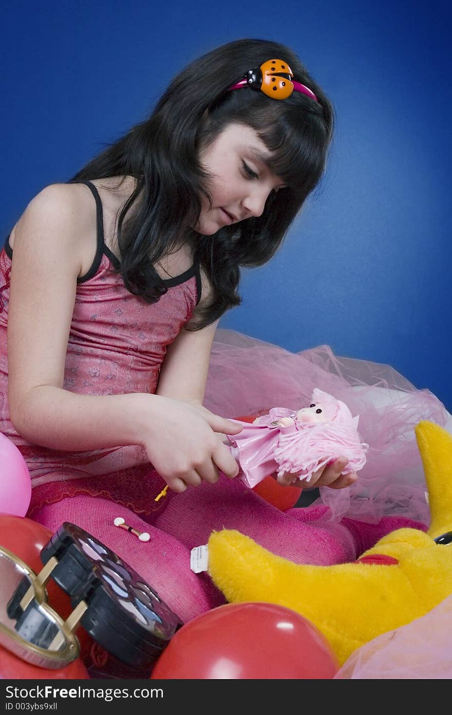 Young and beautiful girl playing with her doll, surrounded by balloons and make up kit