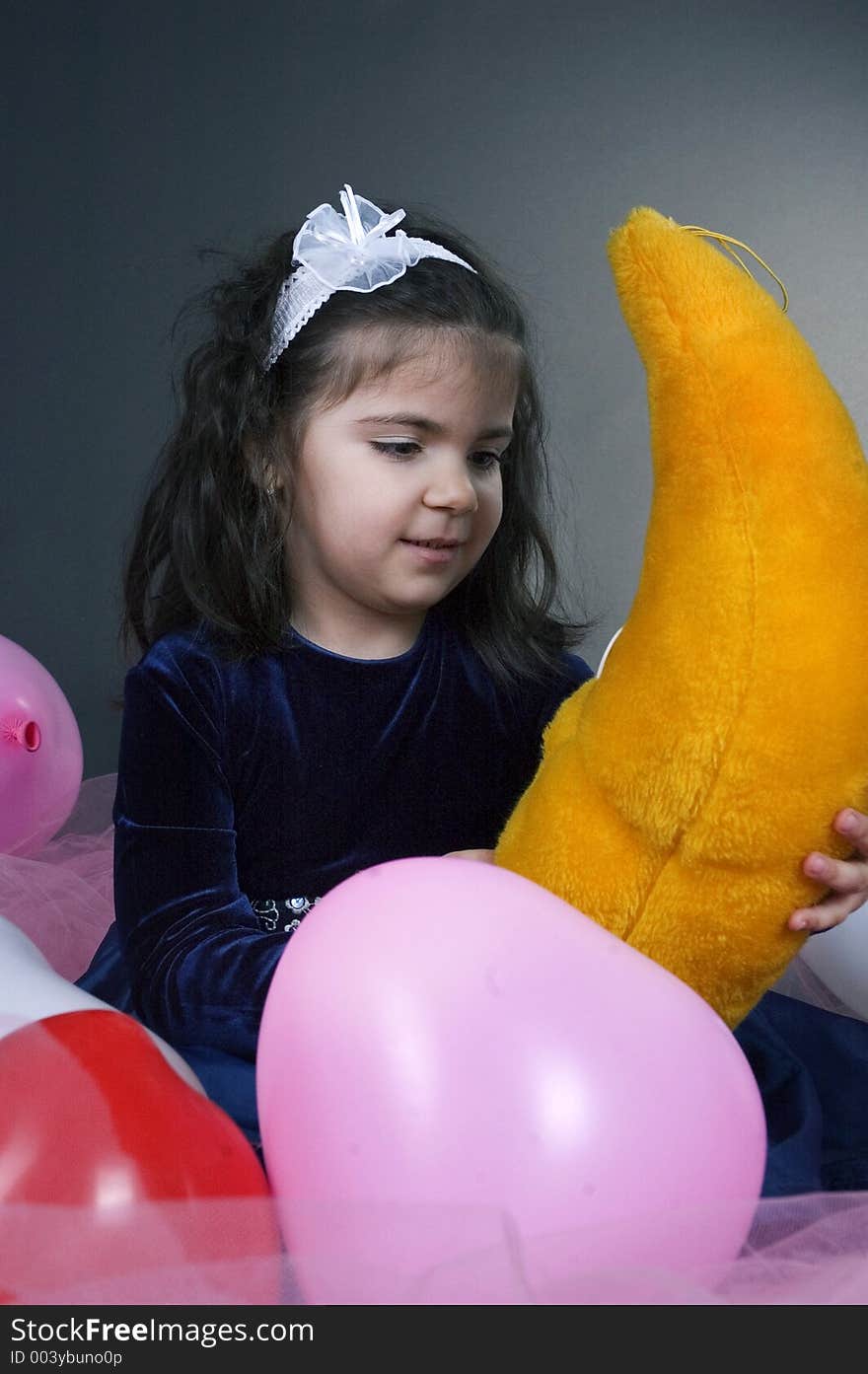 Sweet young girl playing with her plush moon surrounded by coloured balloons