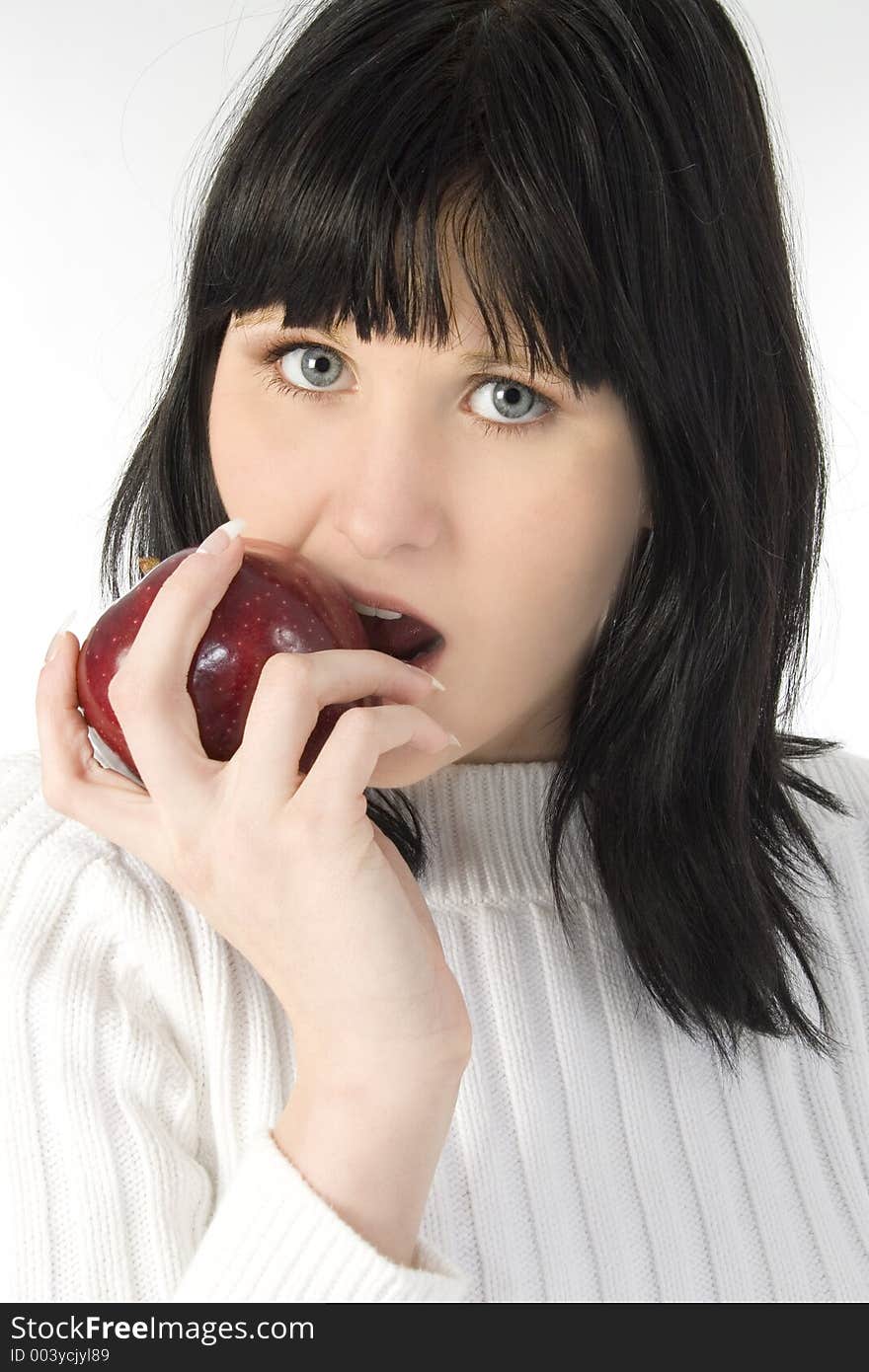 Beautiful young woman in white sweater eating red apple. Shot in studio over white. Beautiful young woman in white sweater eating red apple. Shot in studio over white.