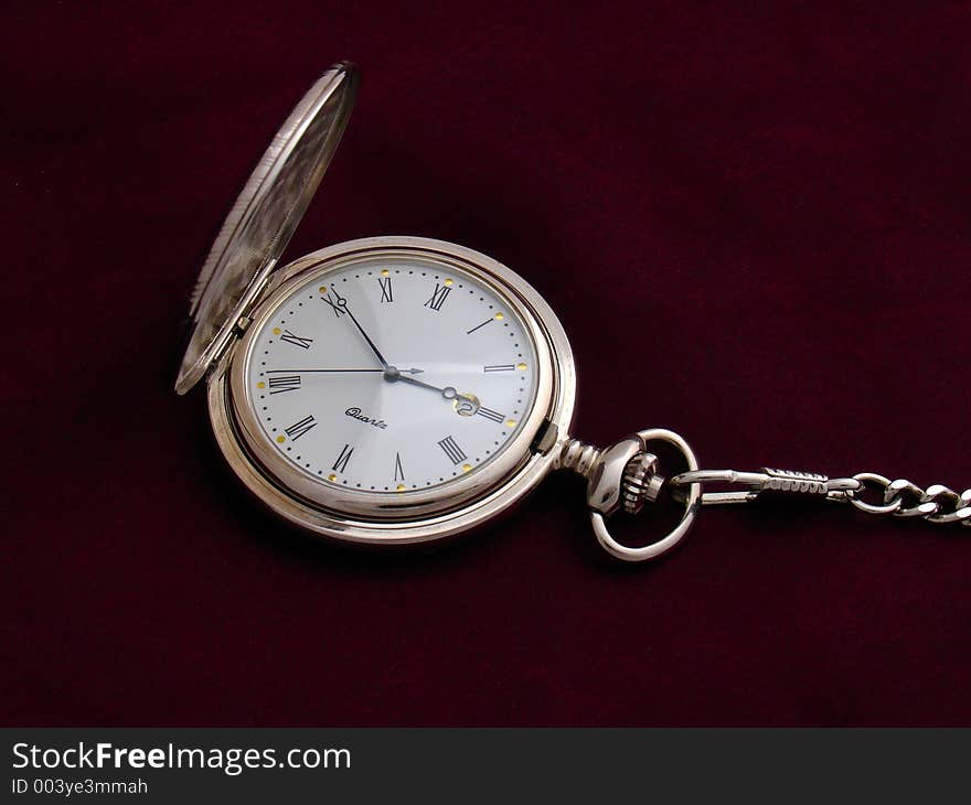 Open silver pocket watch with a chain on purple silk background