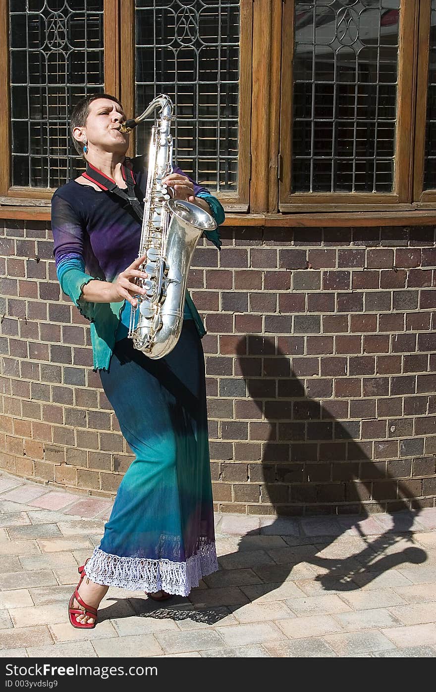 Woman playing saxophone outside with shadow to her left in front of old building. Woman playing saxophone outside with shadow to her left in front of old building.