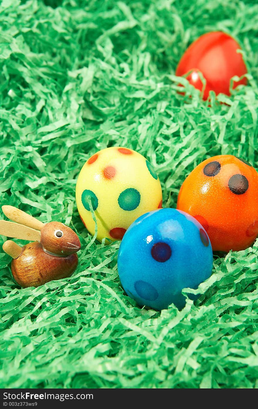 Wooden easter bunny with four coloured easter eggs in green grass