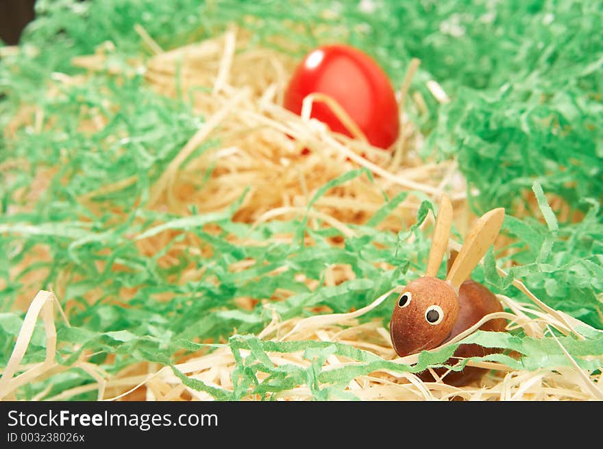 Wooden easter bunny with red easter egg in green grass