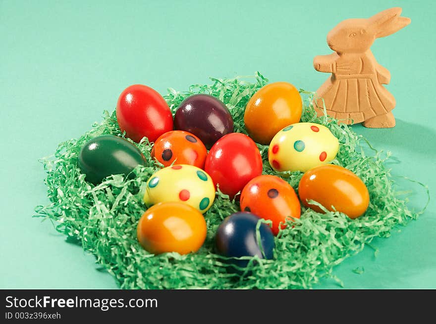 Coloured easter eggs in green grass with ceramic easter bunny on green background