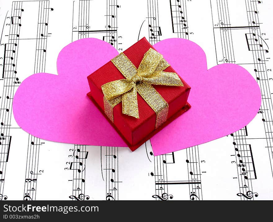 Red giftbox and two pink hearts on music sheet. Red giftbox and two pink hearts on music sheet