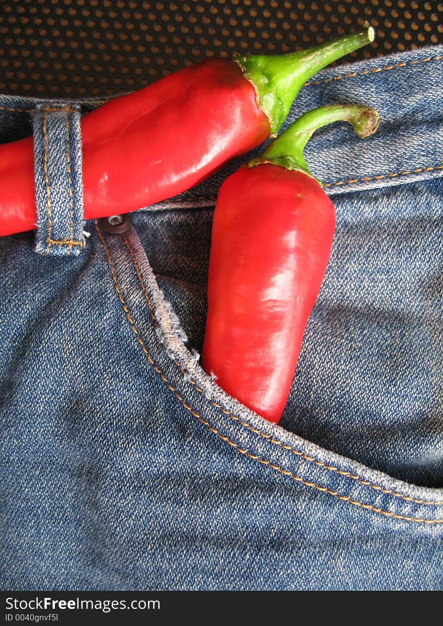 A pair of fashionable hot denim jeans. The red chilies are used as a concept to depict the denim is of the current fashion trend. A pair of fashionable hot denim jeans. The red chilies are used as a concept to depict the denim is of the current fashion trend.