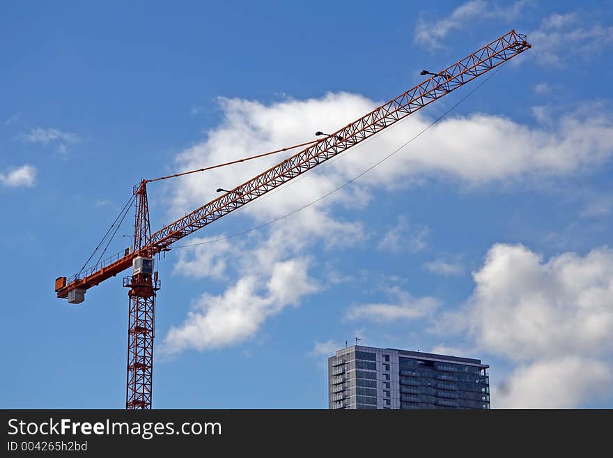 Construction crane and a top of a highrise building on blue sky background with white clouds.