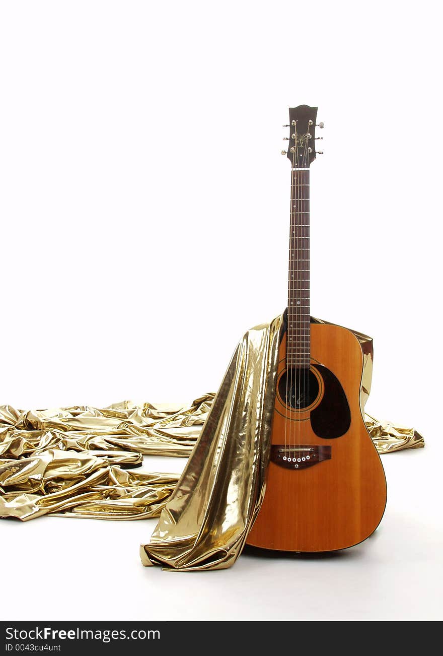 Acoustic guitar with gold material draped over. Acoustic guitar with gold material draped over