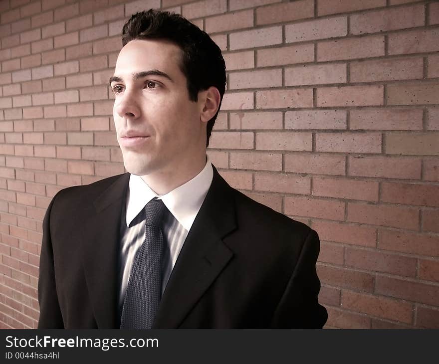 A gentleman stands against a brick wall, looking to the left, showing a feeling of independence. A gentleman stands against a brick wall, looking to the left, showing a feeling of independence.