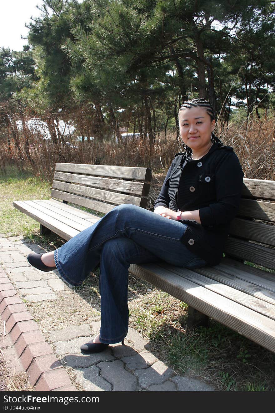 Beautiful Asian girl with braids sitting on a park bench