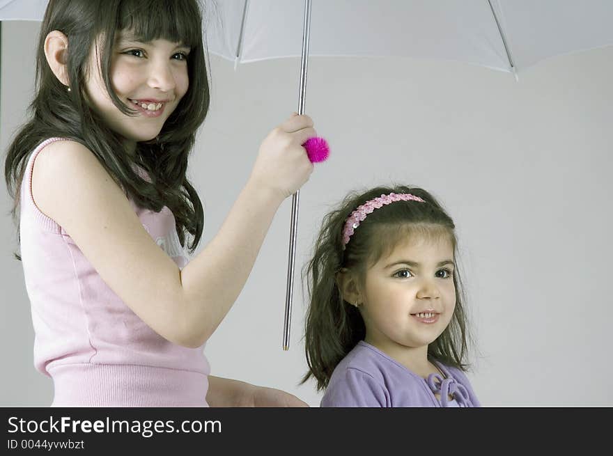 Two little sisters holding an umbrella and smiling happily. Two little sisters holding an umbrella and smiling happily.