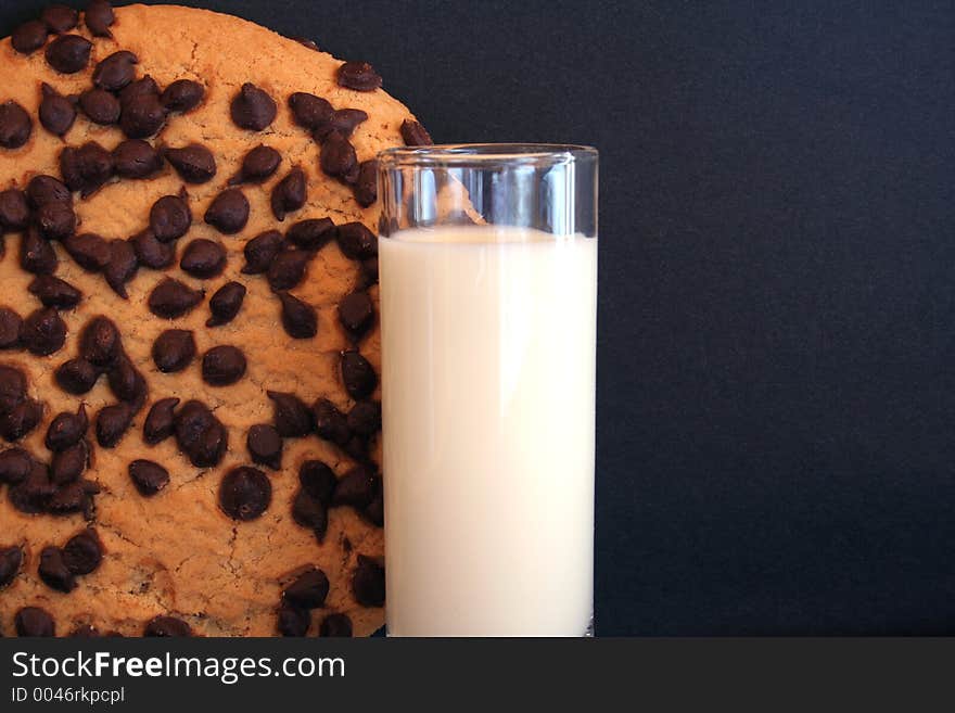 Image of a giant chocolate chip cookie next to a shot glass of milk - room for text. Image of a giant chocolate chip cookie next to a shot glass of milk - room for text